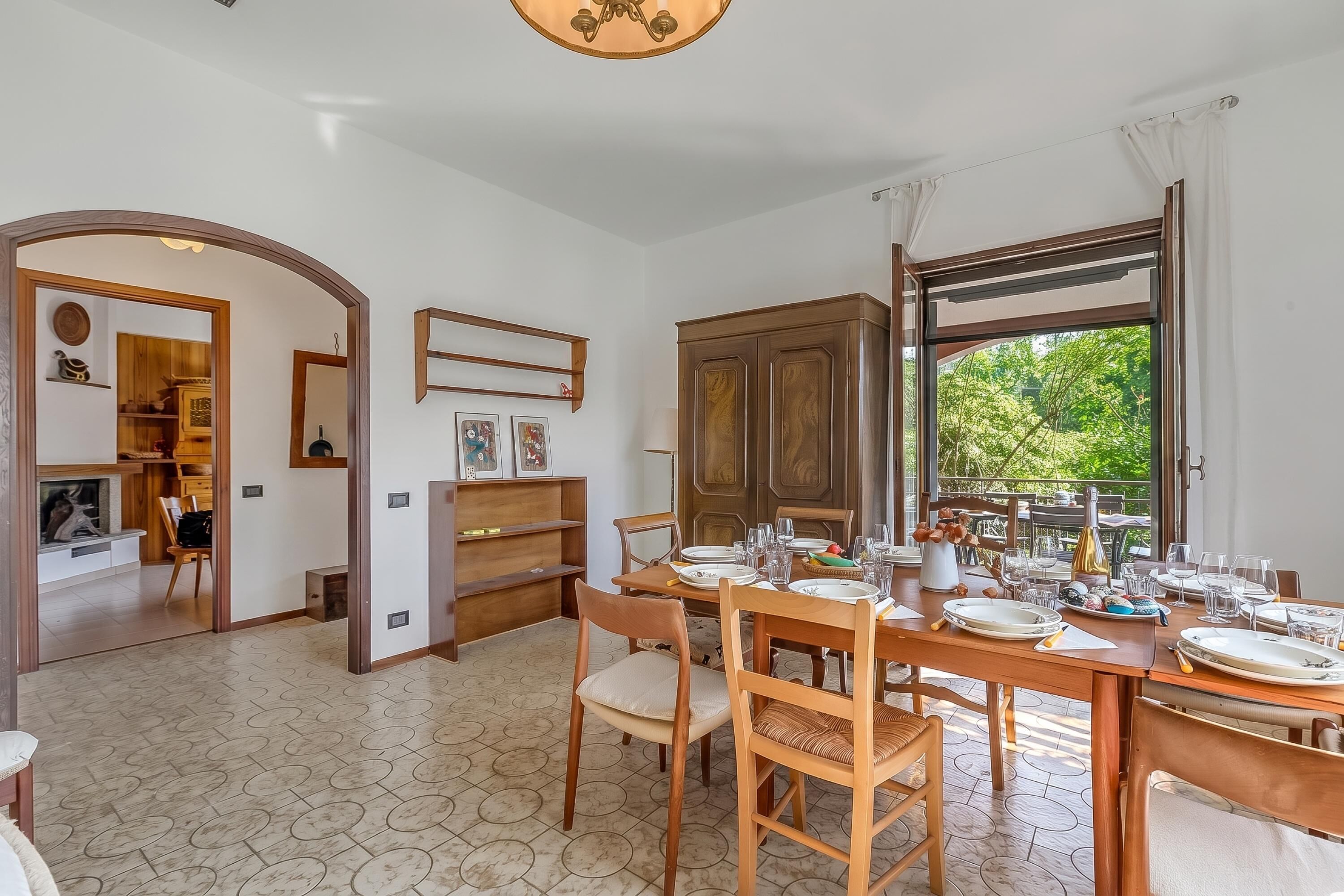 A dining area with a table set for four, a wooden cabinet, and a view of greenery outside.