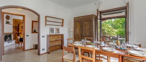 A dining area with a table set for four, a wooden cabinet, and a view of greenery outside.