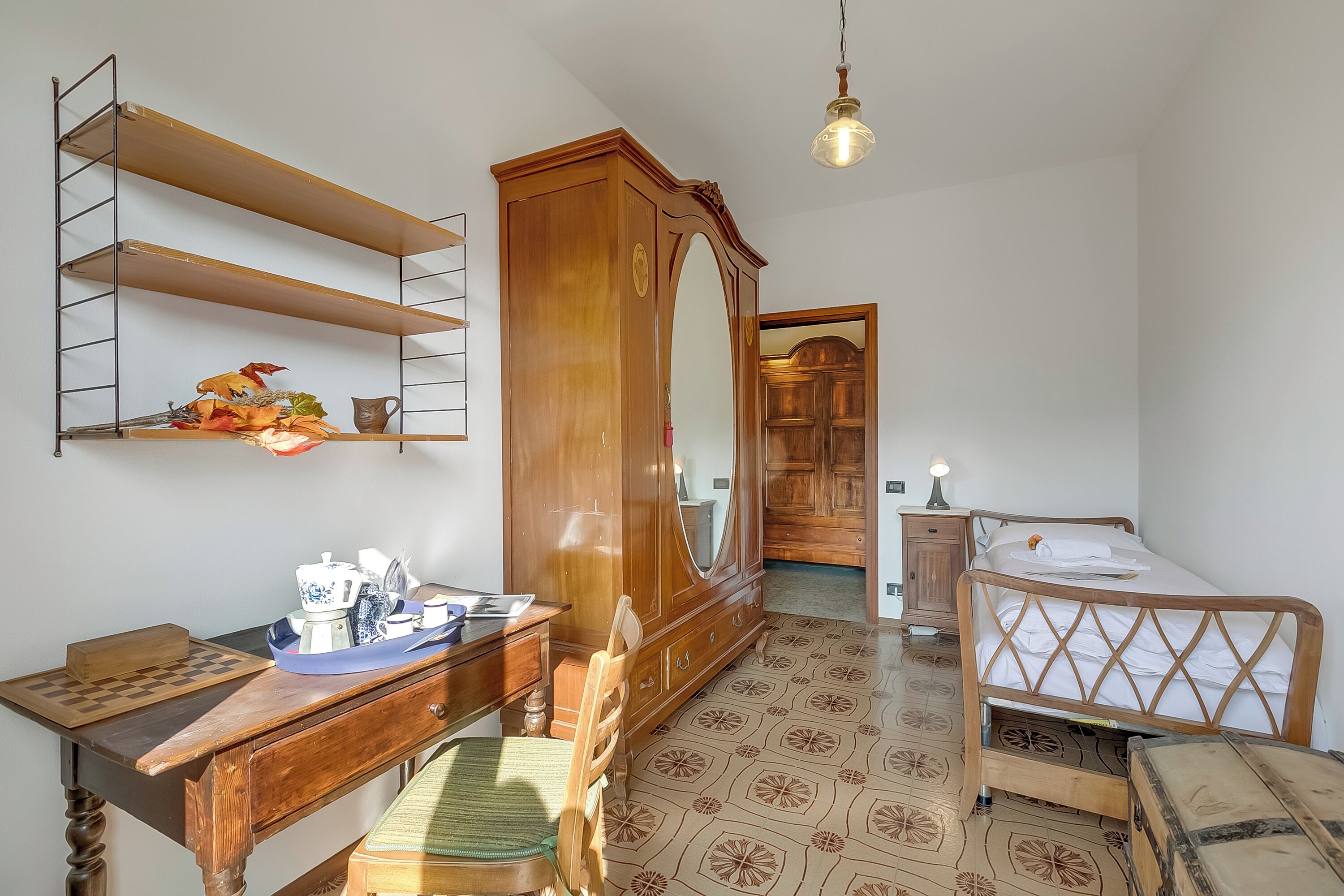 Une chambre avec une armoire en bois, un bureau avec un jeu d’échecs, un lit avec une tête de lit en bois et un plancher à motifs.