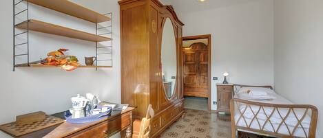 Une chambre avec une armoire en bois, un bureau avec un jeu d’échecs, un lit avec une tête de lit en bois et un plancher à motifs.