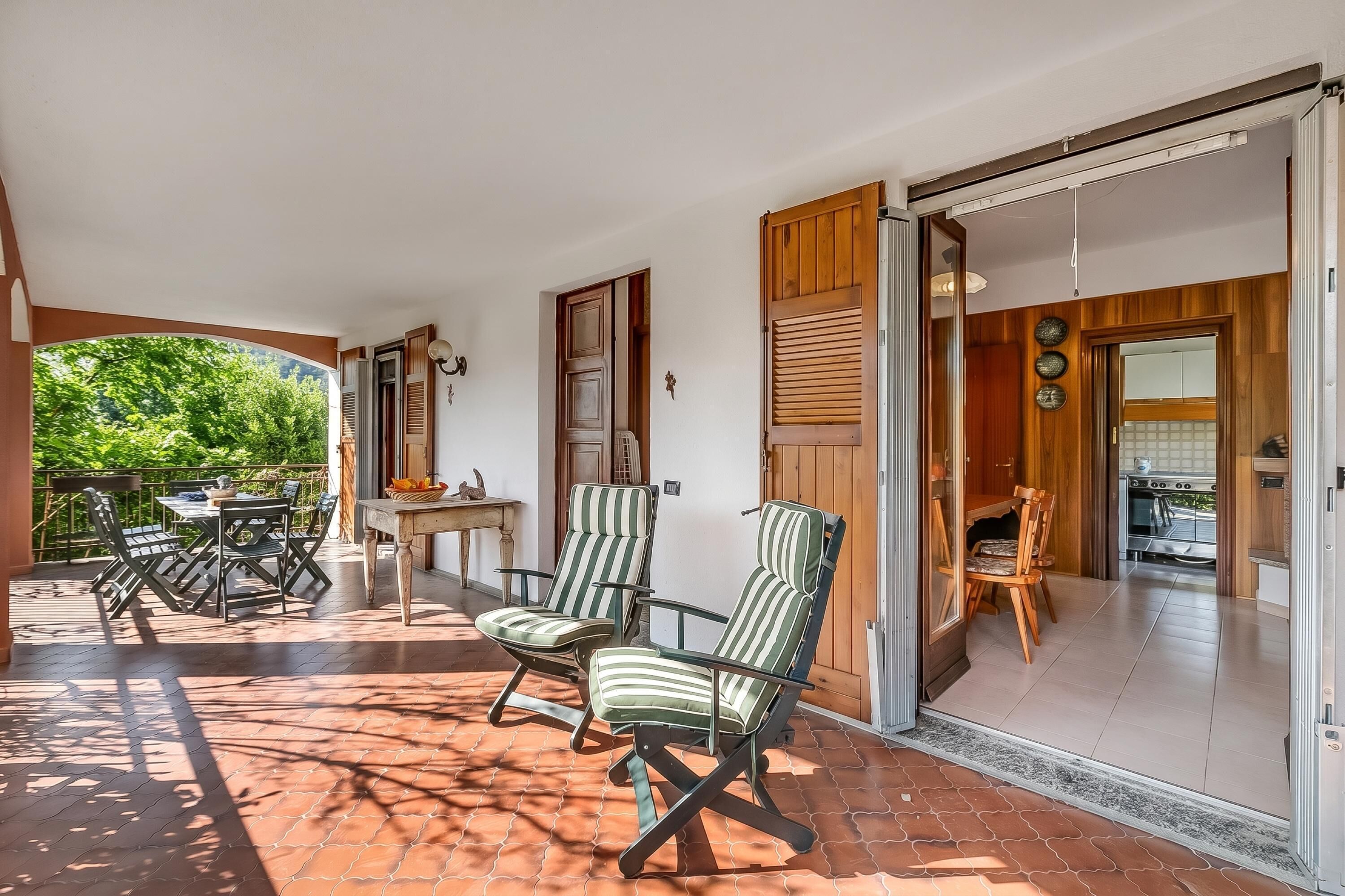 Un patio amueblado con mobiliario exterior, una puerta corrediza que da a una cocina y vistas a zonas verdes.
