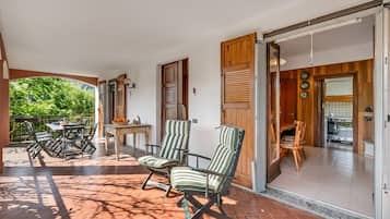 Un patio amueblado con mobiliario exterior, una puerta corrediza que da a una cocina y vistas a zonas verdes.