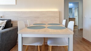 Un espace repas moderne avec une table en bois, quatre chaises et une tête de lit de couleur claire.