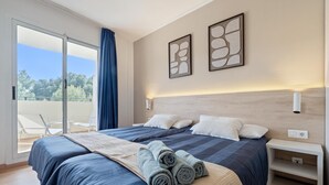 Une chambre d’hôtel moderne avec un grand lit, un balcon avec des chaises et une vue sur les arbres.