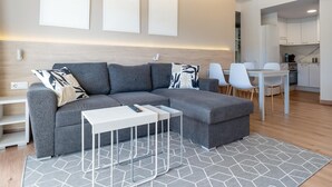Un salon moderne avec un canapé d’angle, une table basse blanche et un coin repas comprenant une table et des chaises blanches.