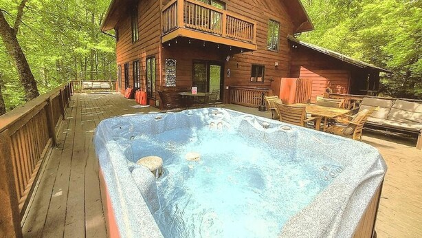 A wooden cabin with a hot tub on a wooden deck surrounded by trees. - Wandering Bear Lodge: Free Tickets /Hot Tub/ Wifi /pool table (Sevierville)