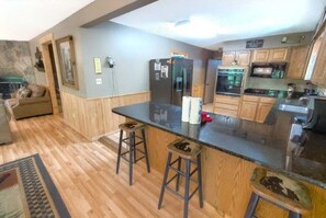 A kitchen with wooden cabinets, a black countertop, and two stools. - Wandering Bear Lodge: Free Tickets /Hot Tub/ Wifi /pool table (Sevierville)