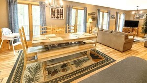 A dining area with a wooden table and chairs, a sofa, and a television. - Wandering Bear Lodge: Free Tickets /Hot Tub/ Wifi /pool table (Sevierville)