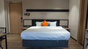Une chambre d’hôtel moderne avec un grand lit, une porte en bois, une petite table et une table de chevet avec une lampe.