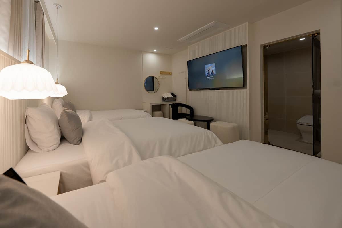 A hotel room with two beds, a TV, a small table, and a bathroom.