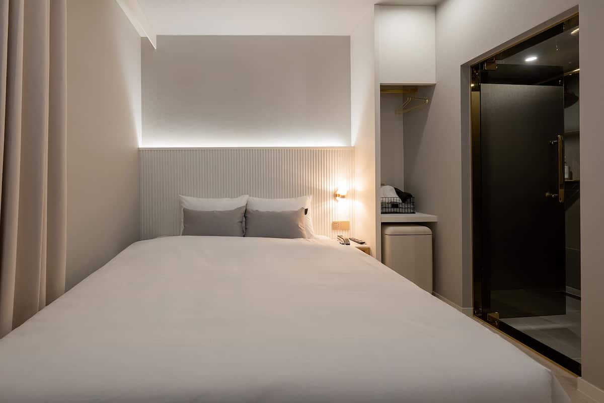 A hotel room with a bed, bedside table, lamp, and a door.