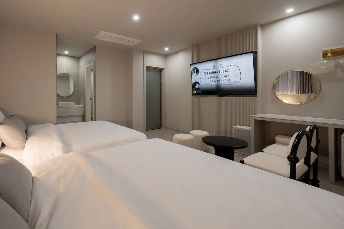 A hotel room with two beds, a TV, a round mirror, a small table, and a seating area.