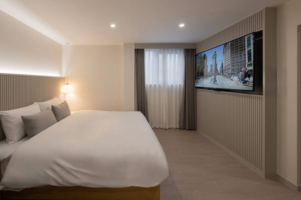 A modern hotel room with a large bed, a television mounted on the wall, and a window with curtains.