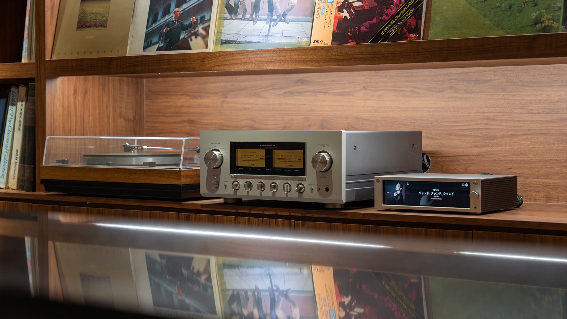 A turntable, a record player, and a small digital device on a wooden shelf.