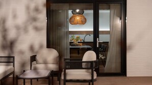 A modern living room with a sofa, a small table, and a chair. There is a sliding glass door leading to a dining area with a table and chairs. - Maison de Denbast (Busan)