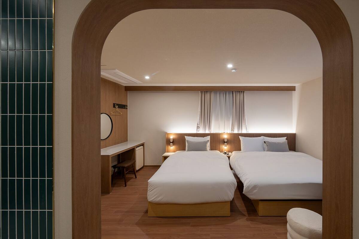 A hotel room with two beds, a desk, a mirror, and a window with curtains.