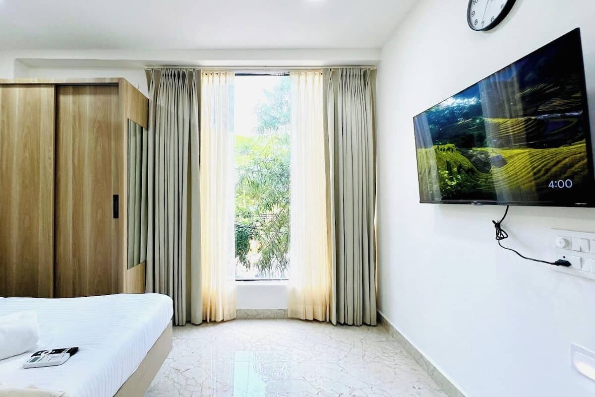 Une chambre d’hôtel avec un lit, une armoire, un téléviseur fixé au mur et une fenêtre avec des rideaux.