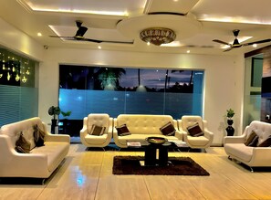 A modern living room with a sofa set, ceiling fans, and a large window with a view. - THE HOTEL RELAX  (Kankavali)