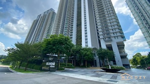 Un edificio residencial de gran altura con diseño moderno, que cuenta con varios balcones y un área circundante bien cuidada con árboles y cielo despejado.