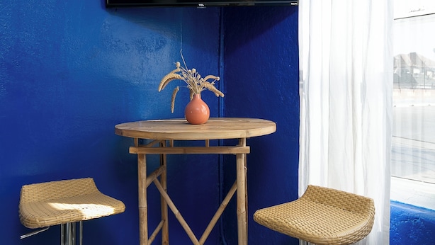 A room with a blue wall, a flat-screen TV mounted above a wooden table, and two wicker bar stools with metal bases.