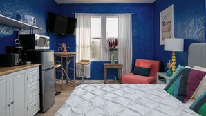 A compact hotel room with a bed, a desk with a computer, a microwave, and a small kitchenette.