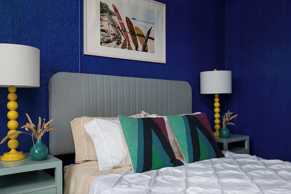A bedroom with a bed, two nightstands, a framed picture, and a blue wall.
