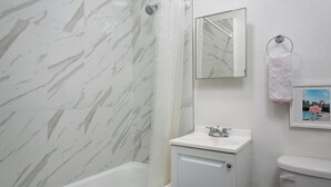 A bathroom with a marble shower wall, a white sink, and a toilet.