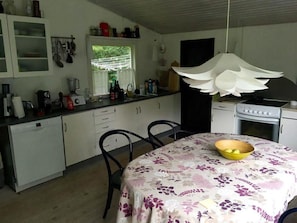 Una cocina con armarios blancos, estufa, lavaplatos y una mesa de comedor con mantel floral.