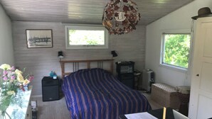 Ein Schlafzimmer mit einem Bett, einem Schreibtisch mit Laptop, einem Heizkörper, einem Fenster und einem Deckenventilator.