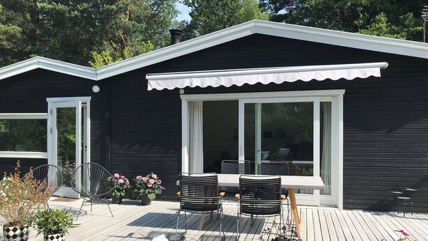 Ein modernes Haus mit einer Terrasse, zwei Stühlen, einem Tisch und Topfpflanzen.