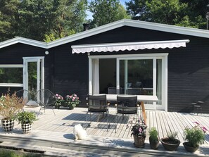 Ein modernes Haus mit einer Terrasse, zwei Stühlen, einem Tisch und Topfpflanzen.