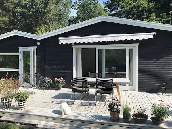 A modern house with a deck, two chairs, a table, and potted plants.