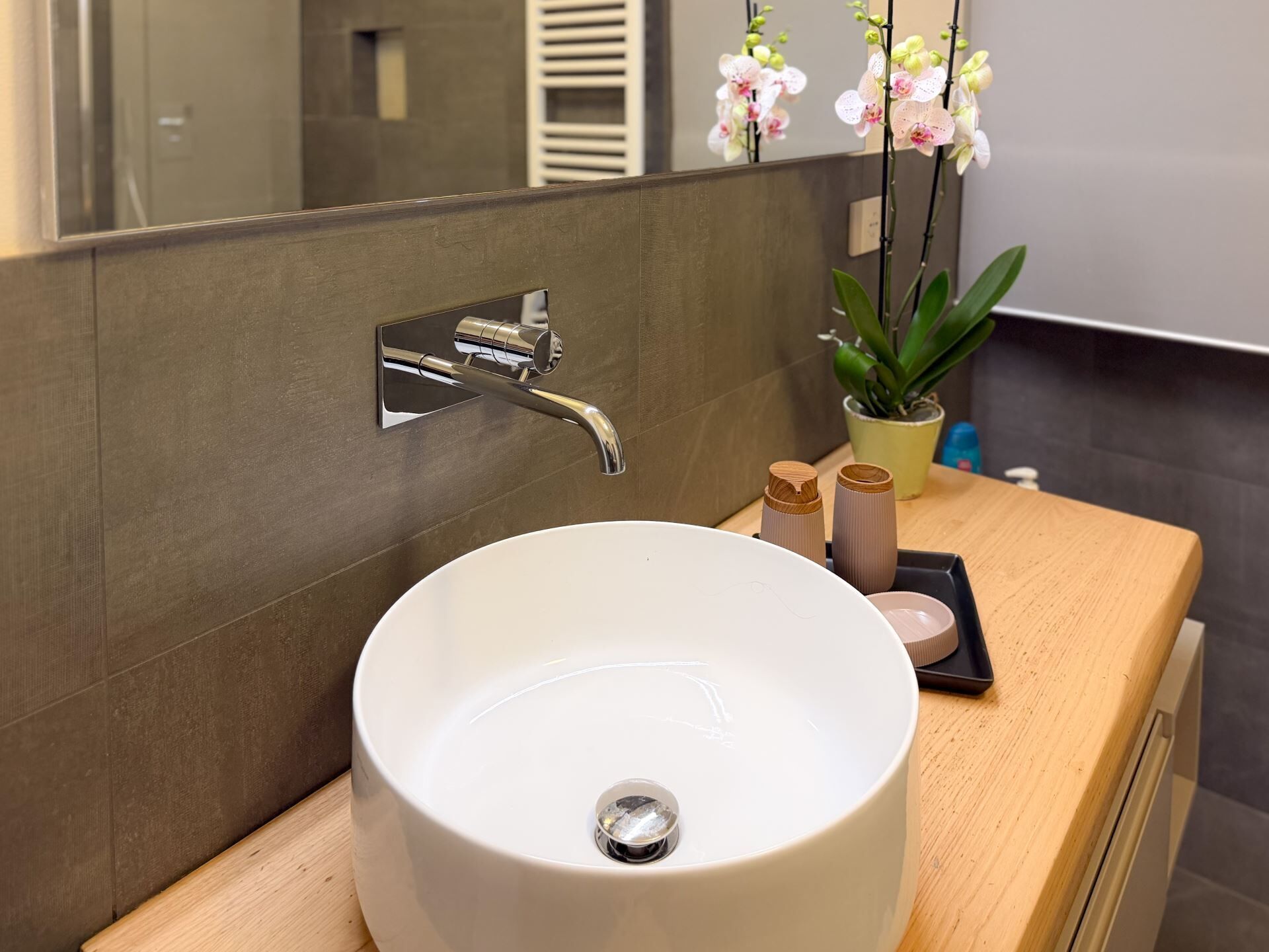 A modern bathroom with a white sink, chrome faucet, and a potted plant.