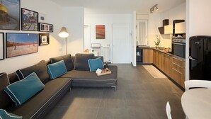 A modern living room with a sectional sofa, a dining table, and a kitchen area with a refrigerator and stove. - Imagine waking up, making coffee, and knowing that the most famous white beaches on Elba Island are (Portoferraio)
