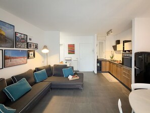 A modern living room with a sectional sofa, a dining table, and a kitchen area with a refrigerator and stove. - Imagine waking up, making coffee, and knowing that the most famous white beaches on Elba Island are (Portoferraio)