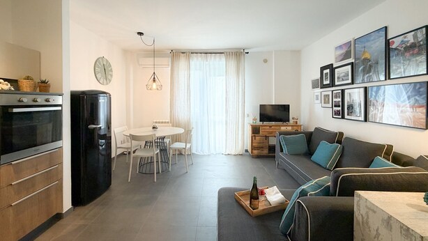 A modern living room with a sofa, a coffee table, and a TV. There is a dining area with a table and chairs. The kitchen has a stove and a refrigerator. - Imagine waking up, making coffee, and knowing that the most famous white beaches on Elba Island are (Portoferraio)