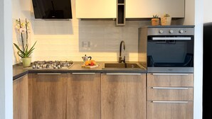 A modern kitchen with wooden cabinets, a gas stove, a sink, and an oven. - Imagine waking up, making coffee, and knowing that the most famous white beaches on Elba Island are (Portoferraio)