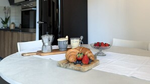 A breakfast setting with a croissant, strawberries, blueberries, a coffee pot, and a cup labeled "Cafe" on a table. - Imagine waking up, making coffee, and knowing that the most famous white beaches on Elba Island are (Portoferraio)