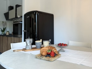 A breakfast setting with a croissant, strawberries, blueberries, a coffee pot, and a cup labeled "Cafe" on a table. - Imagine waking up, making coffee, and knowing that the most famous white beaches on Elba Island are (Portoferraio)