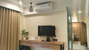 A hotel room with a flat-screen TV, a wooden desk, a potted plant, and an air conditioning unit. - HOTEL ABHIJIT (Uluberiya)