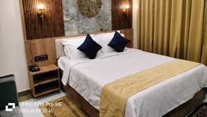 A hotel room with a wooden headboard, a large wall-mounted artwork, a bed with white bedding and two pillows, a bedside table with a phone, and a curtain on the window. - HOTEL ABHIJIT (Uluberiya)