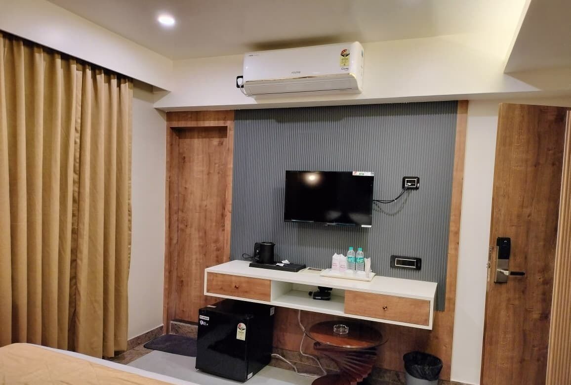 Una habitación de hotel moderna con un televisor de pantalla plana montado en una pared gris, un mueble de madera debajo y una cafetera pequeña.