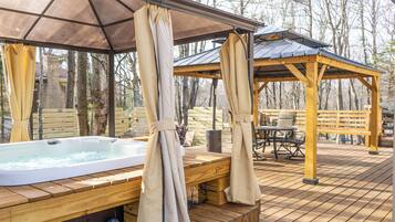 A wooden deck with a hot tub, wooden benches, and a gazebo.
