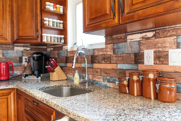 A kitchen with wooden cabinets, a granite countertop, and a sink. There are jars with wooden lids on the counter.