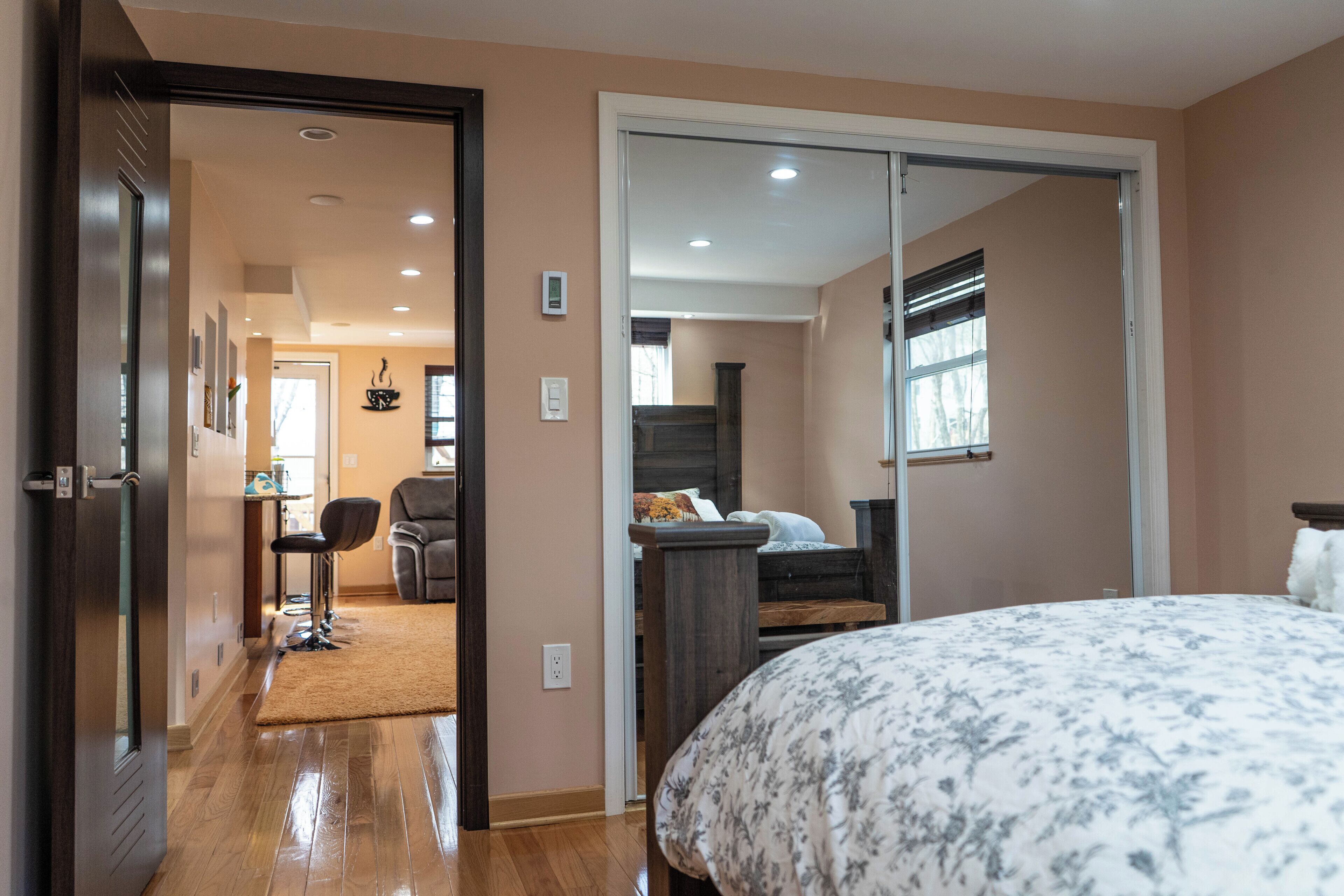 A bedroom with a large bed, a wooden floor, a door leading to a bathroom, and a view of a staircase.