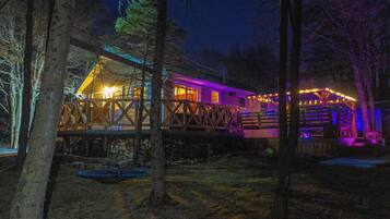 A wooden cabin with a deck, surrounded by trees.
