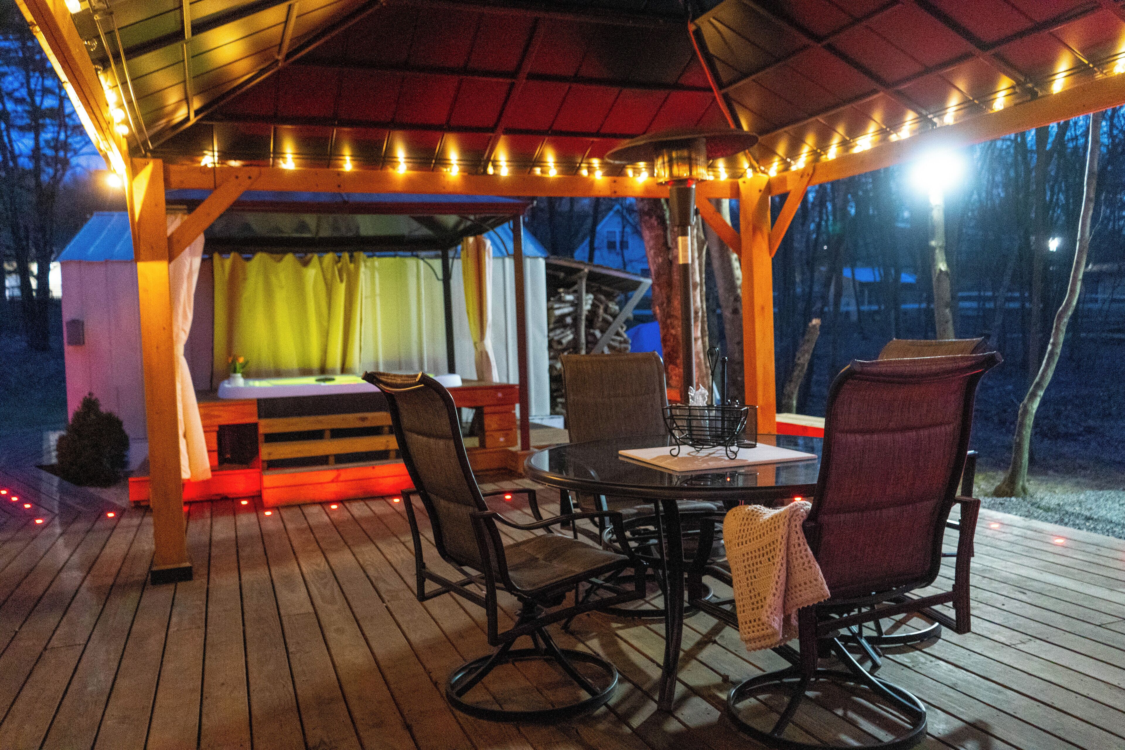 An outdoor wooden deck with a covered seating area, featuring a table and chairs, and string lights.