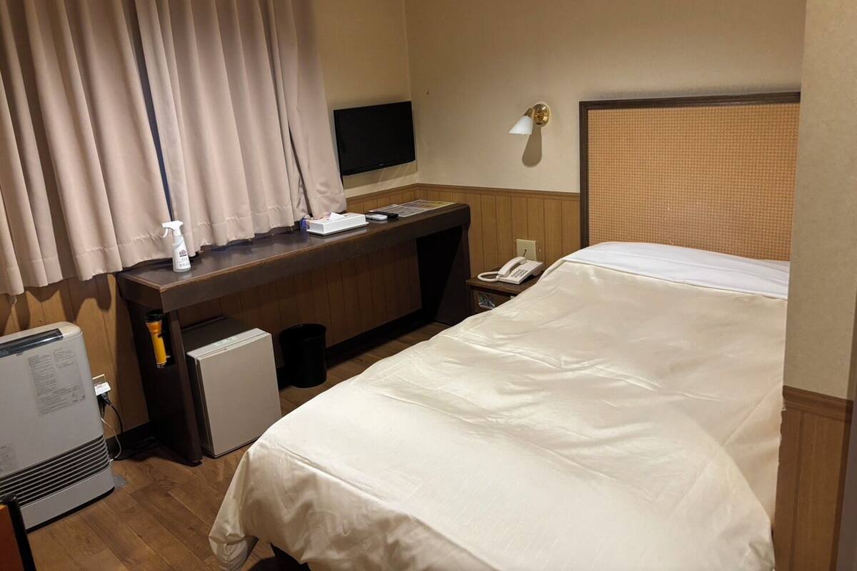 A hotel room with a bed, a desk with a computer, a TV, a phone, and an air conditioner.