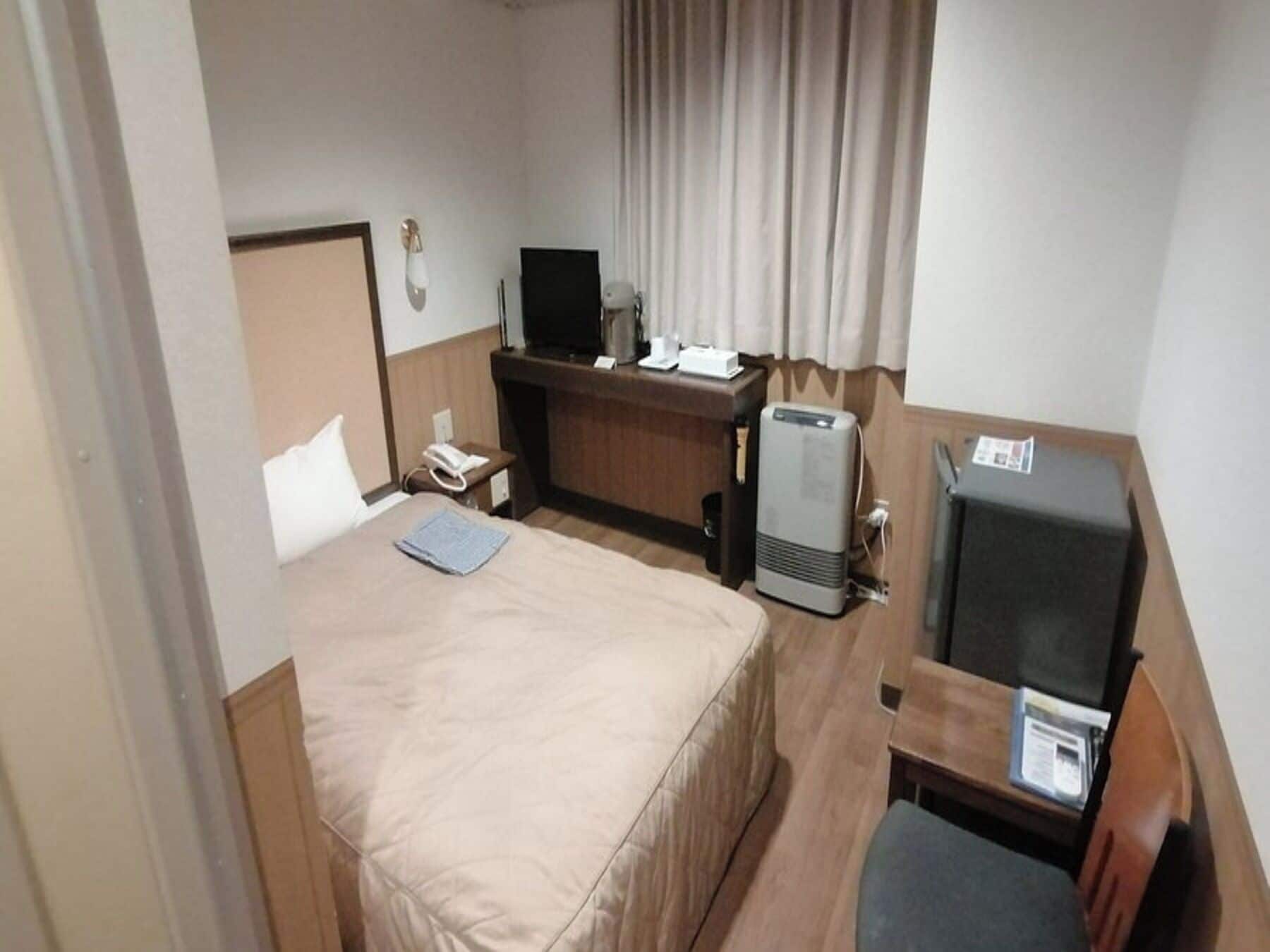 A hotel room with a bed, desk, television, and a small seating area.