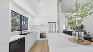 A modern kitchen with white cabinetry, a stainless steel refrigerator, and a large window.